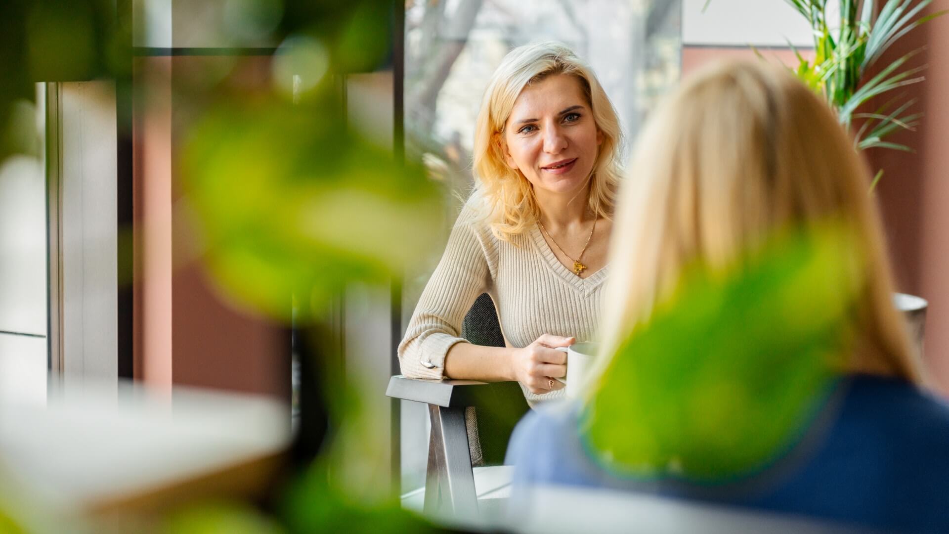 Two women talking with plants in the foreground in the Gdansk office in Poland. 