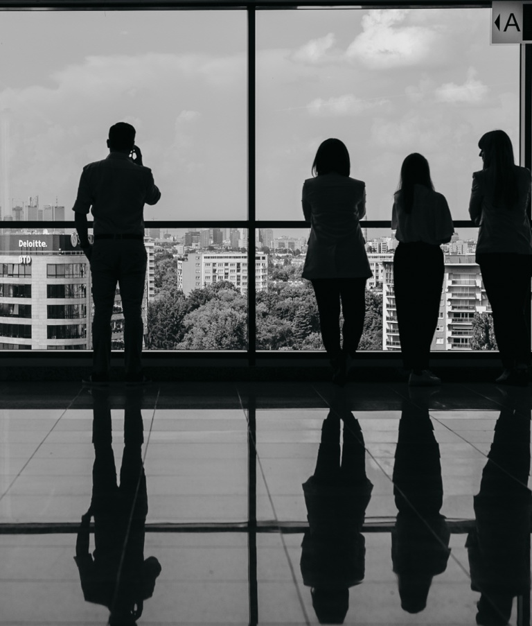 Black and white silhouettes of people in the Warsaw office in Poland looking out a large window.