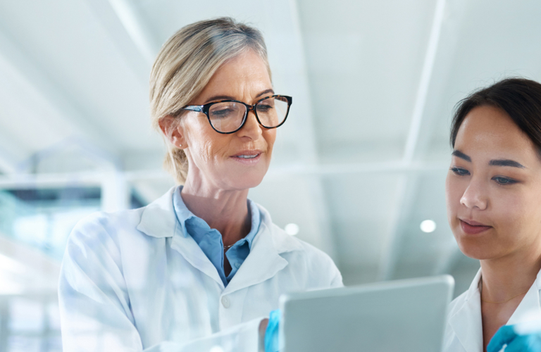 Two scientists in lab coats and gloves reviewing data on a digital tablet in a laboratory environment – illustrating collaboration, data integration, and digital workflows in the life sciences sector.