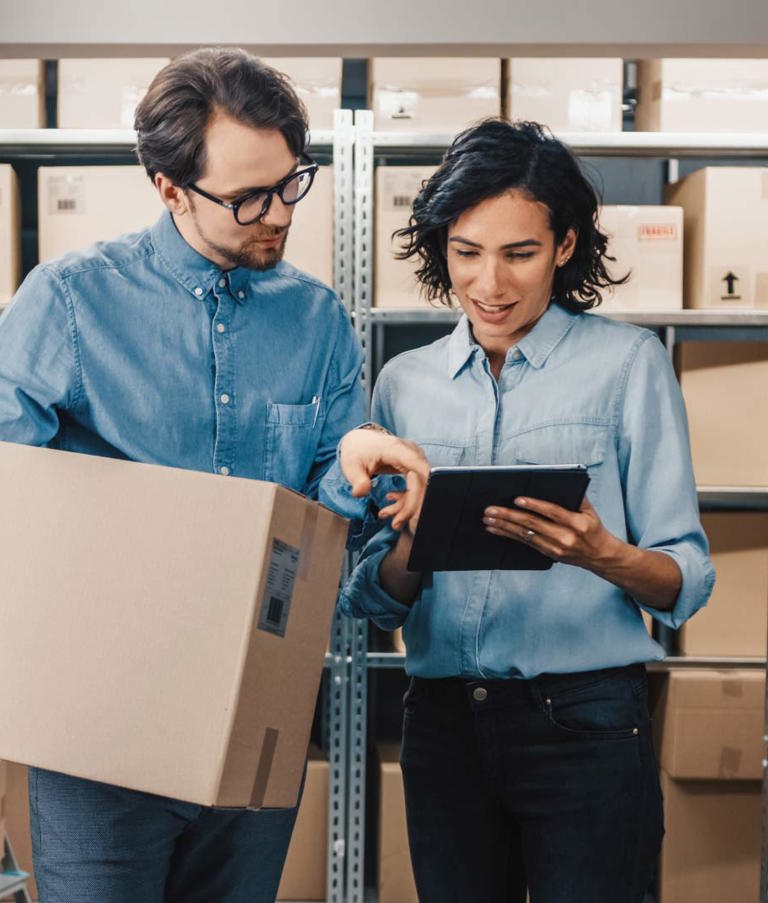 Warehouse employees checking inventory data while managing packages efficiently