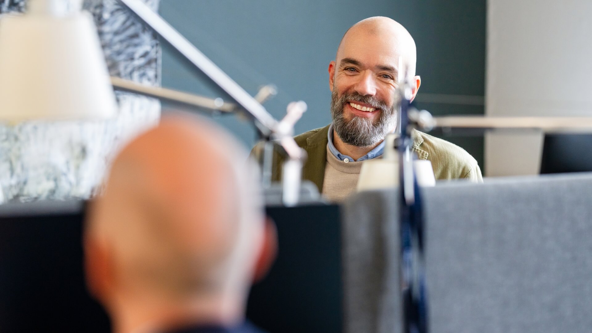 Man in front of computer, smiling at another man in the Copenhagen office in Denmark. 