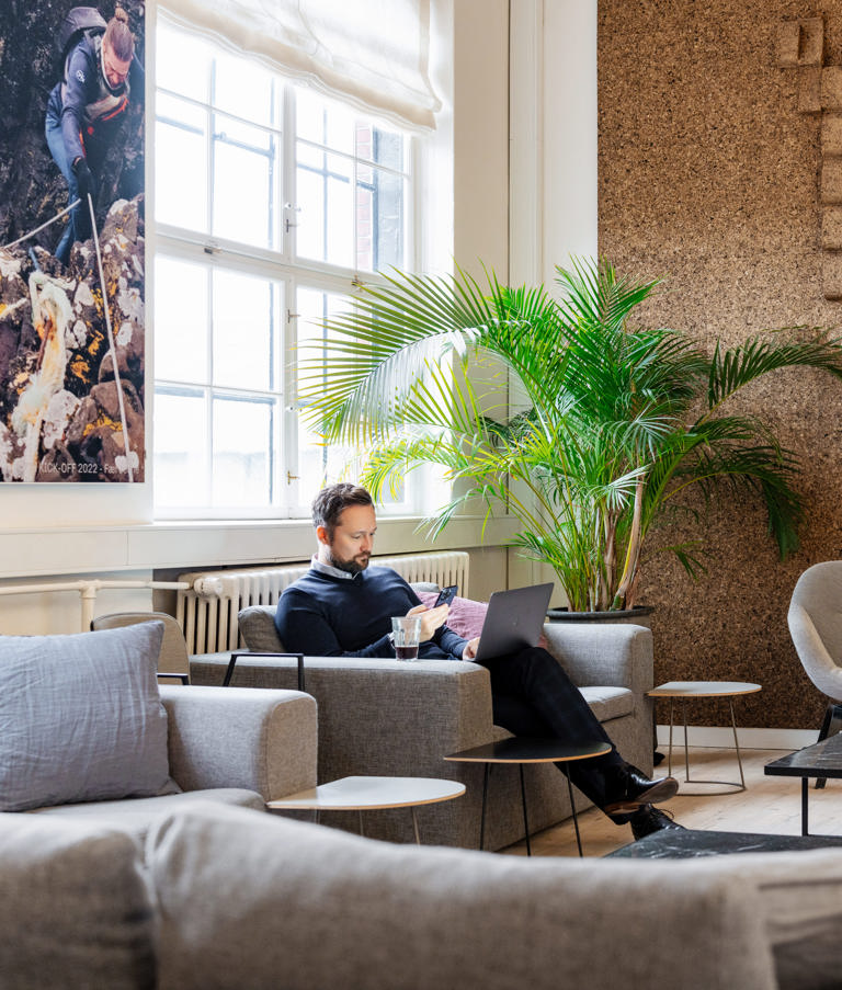 Man sitting with a computer looking at his phone in the Copenhagen office in Denmark