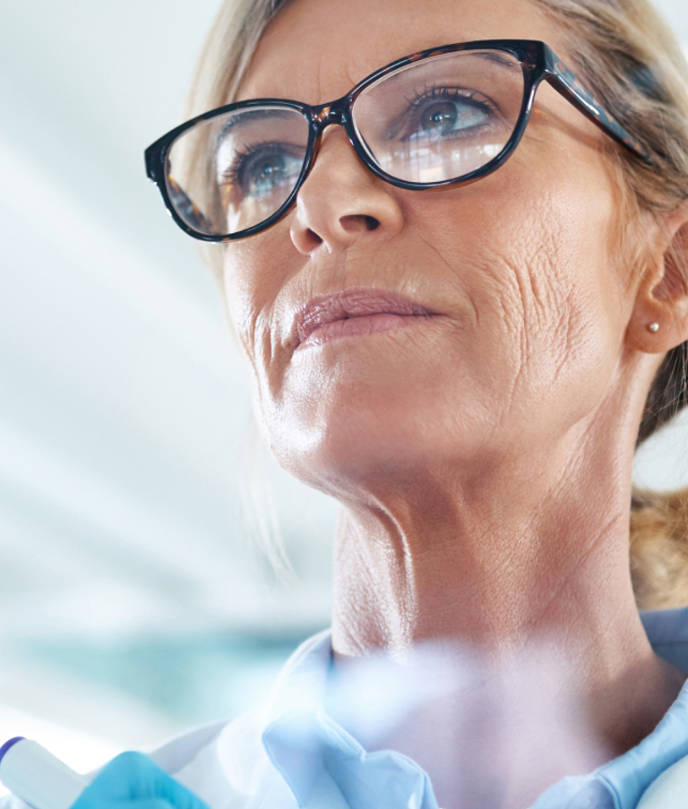 Scientist wearing a lab coat and glasses, analyzing chemical formulas on a transparent board in a laboratory setting – representing data-driven processes and digital innovation in the life sciences sector.