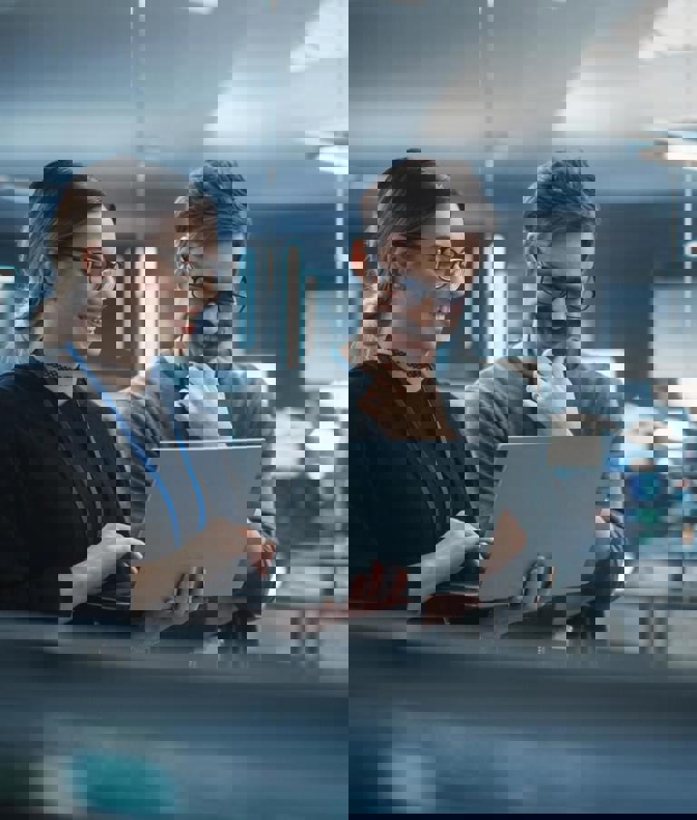 Two smiling people looking at a computer in a workshop