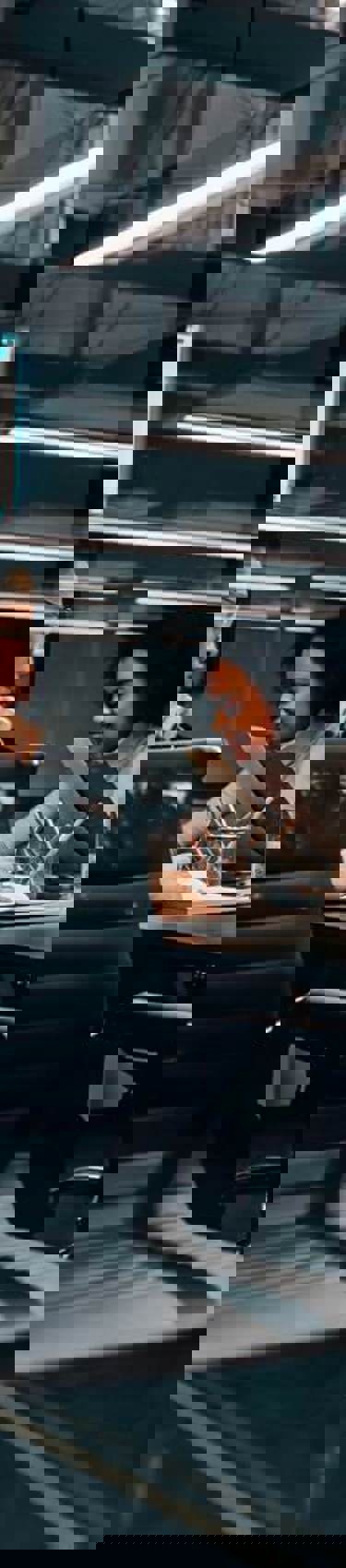 Six people in a meeting room with an industrial feel and statistics on a screen