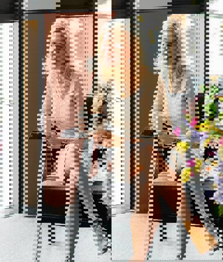 Two women sitting in a grey chairs with a cup of coffee talking