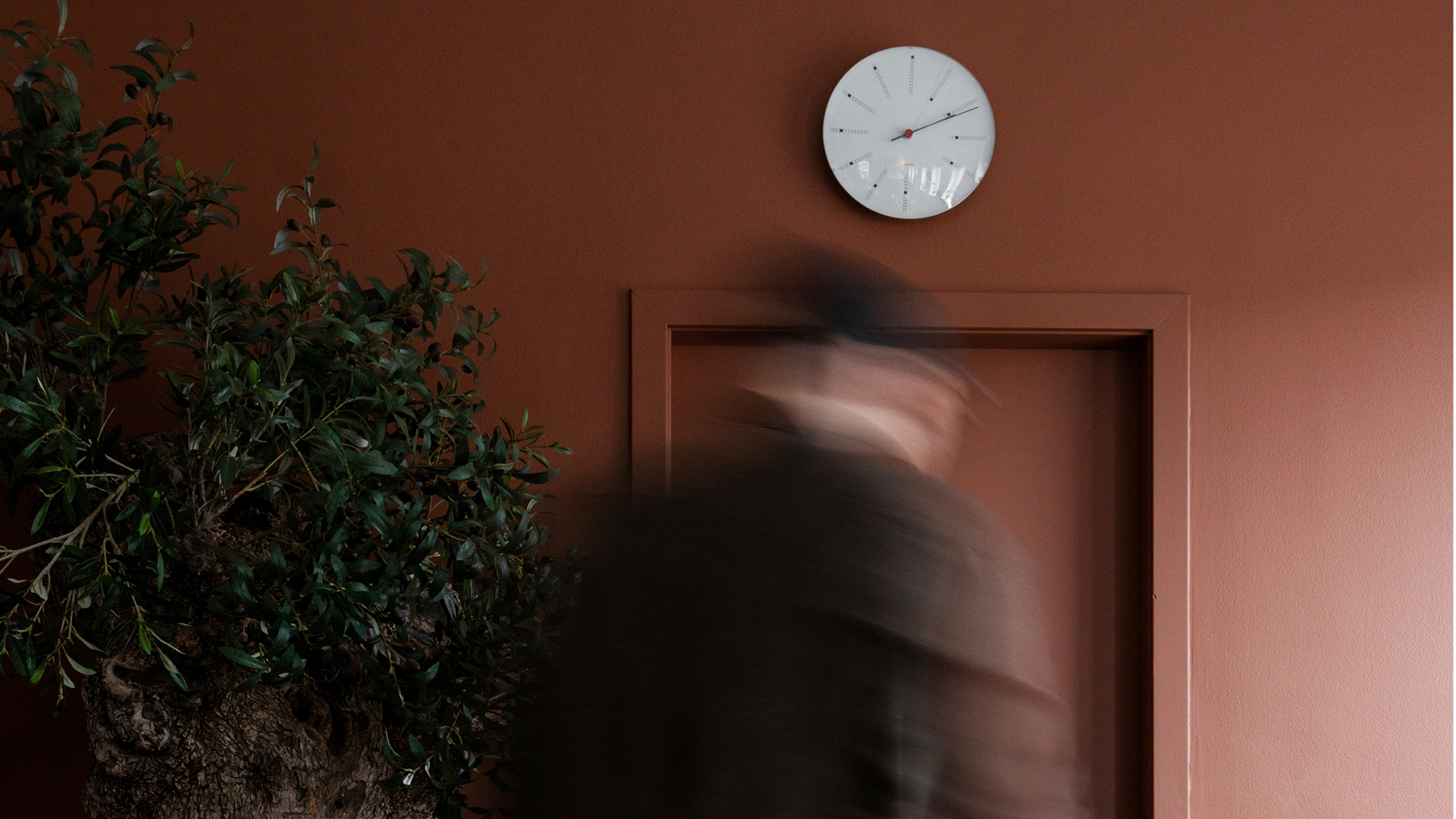 Man walking towards a clock on a red wall in the Copenhagen office in Denmark 